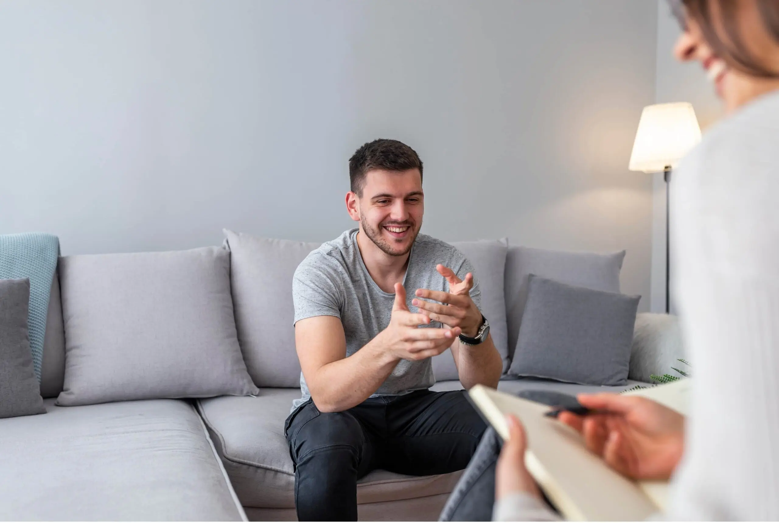 Man in therapy session sitting on couch smiling and gesturing with hands Mental health and wellness concept