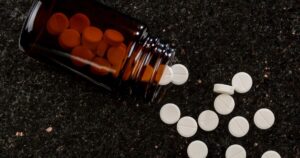 Brown glass bottle tipped on a dark speckled surface with white round tablets spilled out nearby
