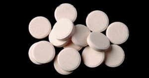 Pile of white circular tablets scattered on a black background close up view