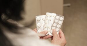 Close up of hands holding several blister packs of white pills