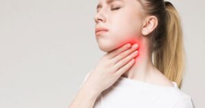 Young woman with a pained expression touching her red sore throat area on her neck