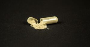 A two piece translucent capsule broken in half with beige powder spilled on a dark surface