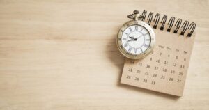 Vintage brass pocket watch resting on a small spiral calendar on a light wooden surface