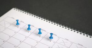 Open spiral calendar with blue pushpins marking several dates across the month