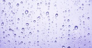Close up of numerous raindrops clinging to a purple tinted glass surface