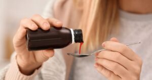 Person pouring red liquid from a dark bottle into a spoon in a closeup shot
