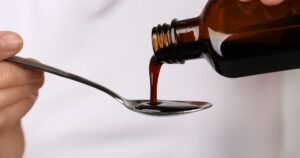 Dark viscous brown liquid being poured from a bottle into a metal spoon held by a hand