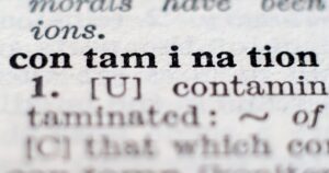 Close up of a dictionary page showing the word contamination in bold with related form contaminated nearby in a macro photograph at a shallow depth of field