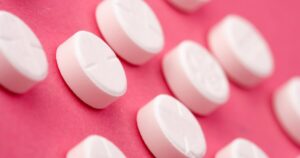 Close up of white round pills scattered on a pink surface