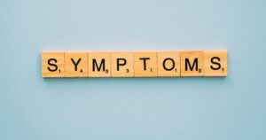Scrabble style letter tiles spell the word SYMPTOMS on a light blue background