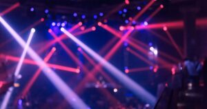 Blurred nightclub scene with bright red and purple laser lights crisscrossing above a DJ booth or stage