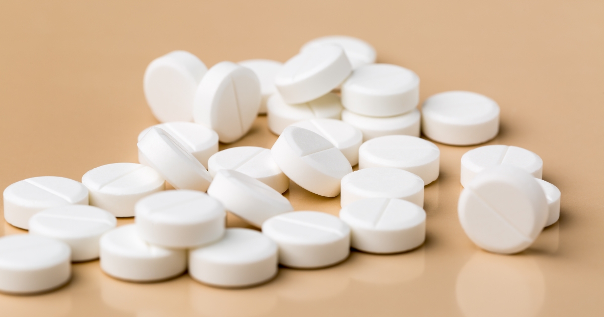 White round tablets scattered on a beige surface showing a mix of lying and stacked pills
