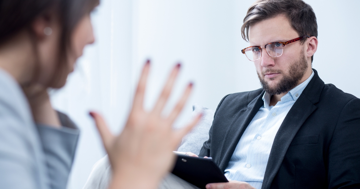 Two professionals in a discussion a bearded man with glasses in a blazer holds a tablet facing a blurred speaking partner
