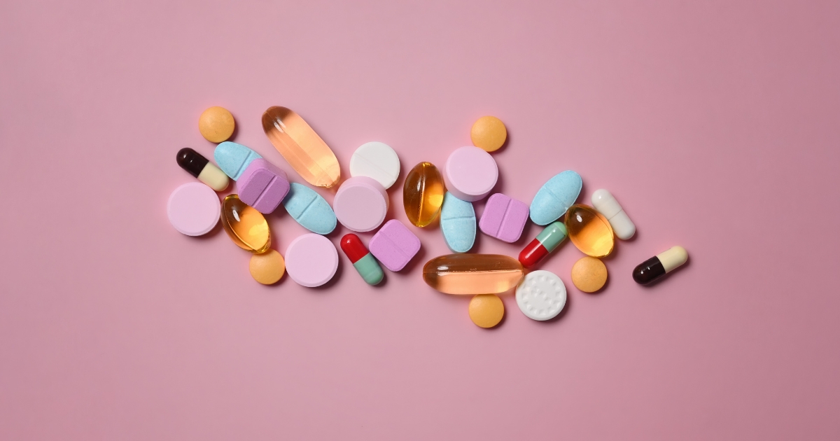Assorted colorful pills and capsules scattered on a pink background