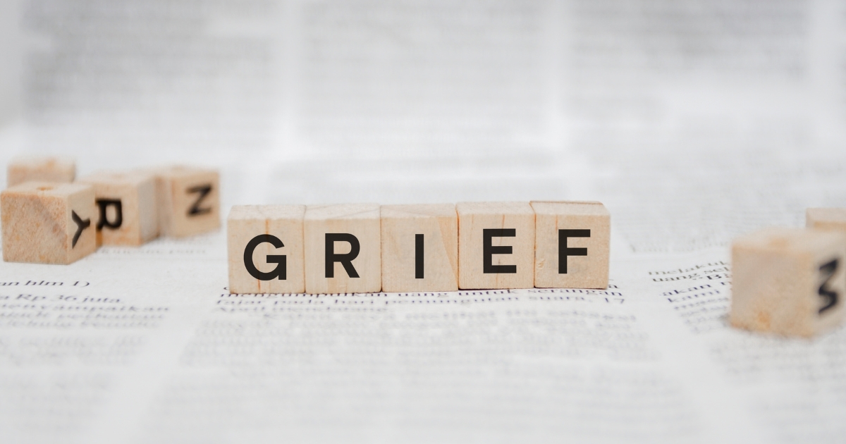 Wooden letter blocks spell GRIEF on a blurred newspaper background