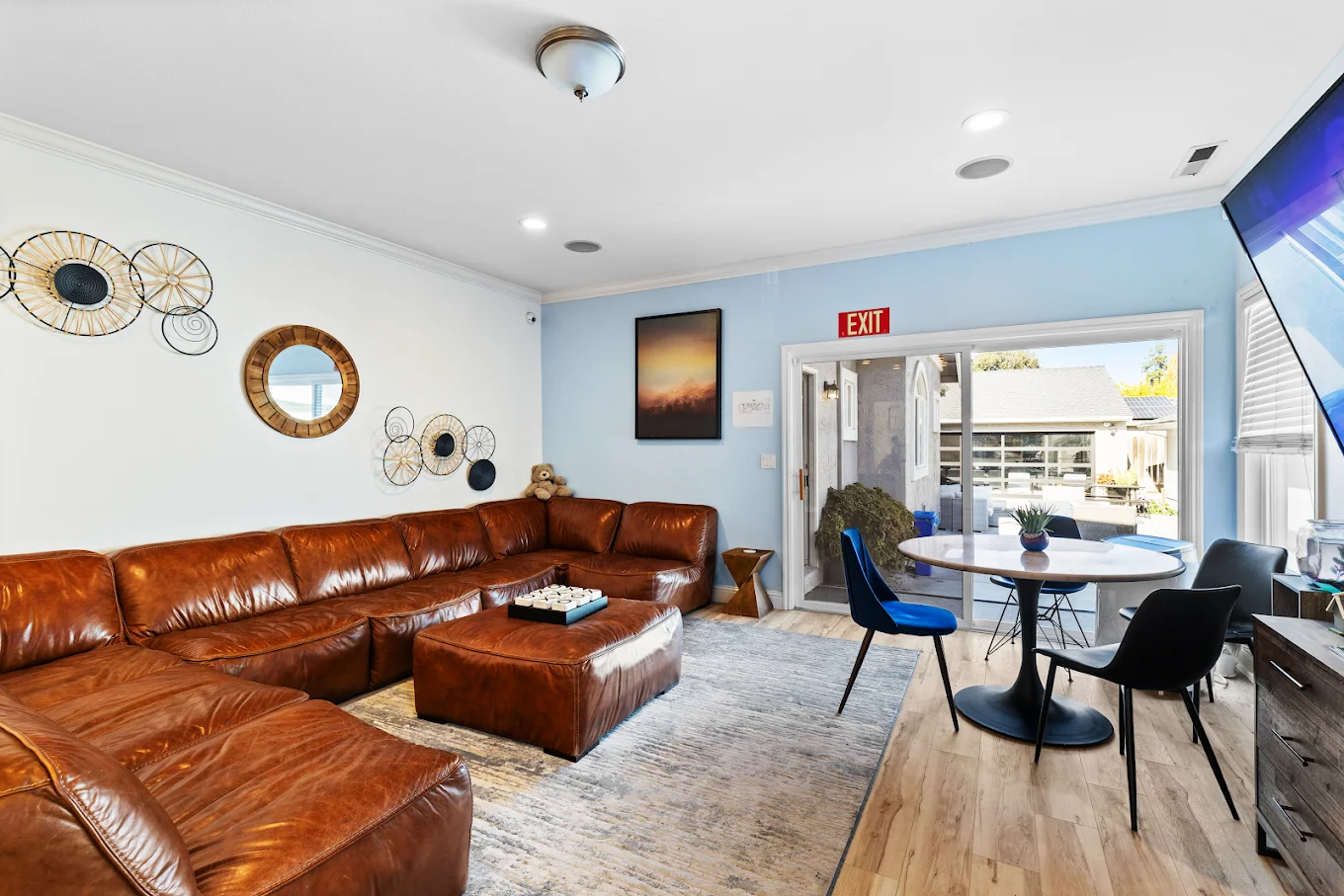 Cozy living room with a large brown leather sectional round coffee table and light wood floors blue accent wall and doorway to outside patio