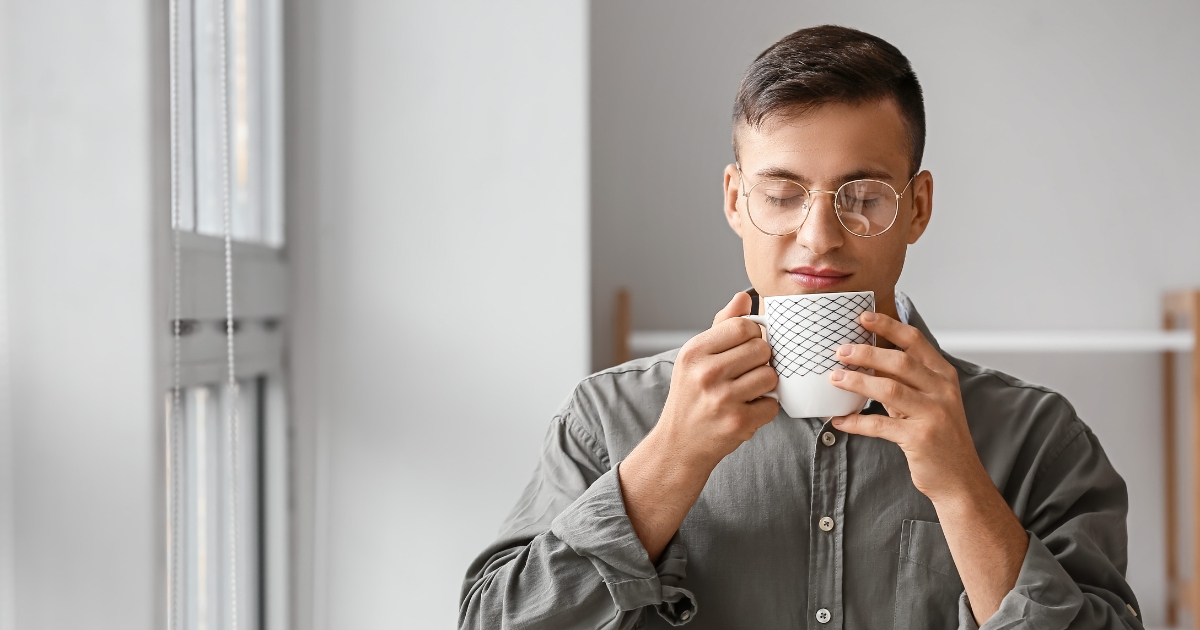 Man with round glasses sipping a mug with a geometric pattern in a bright minimalist room