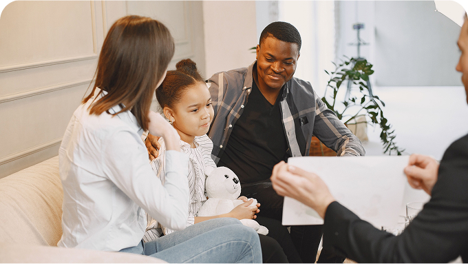 Family of three sitting on a couch with a counselor child holding a white stuffed panda looking at a document