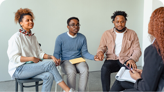 Four diverse adults sit in a circle holding hands during a group discussion or support session