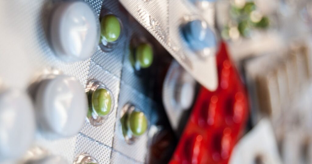 Blister packs of green pills with white and blue capsules angled on a surface with a blurred background