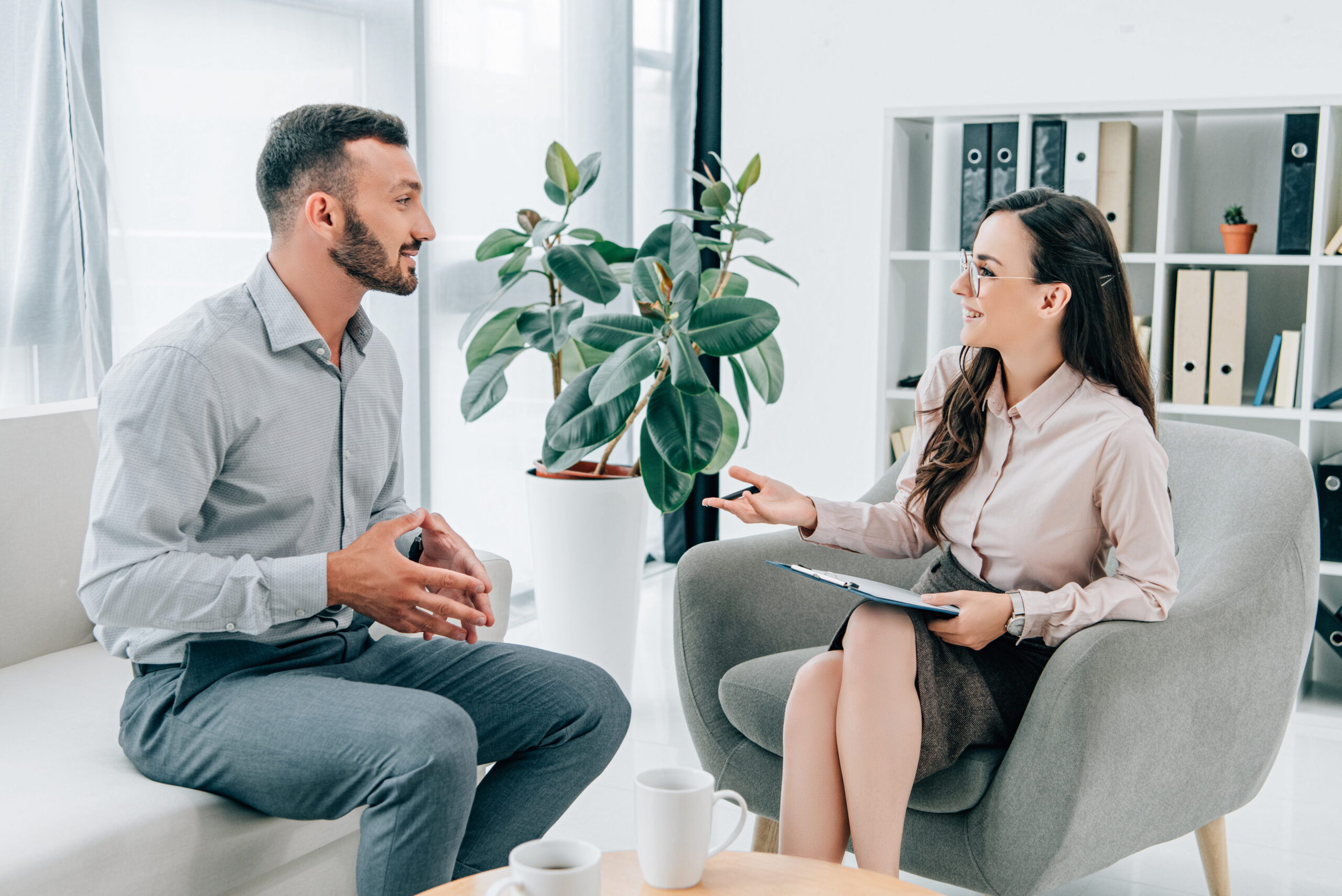 Two professionalsman on the left and woman on the righttalking in a bright office with a large plant between them