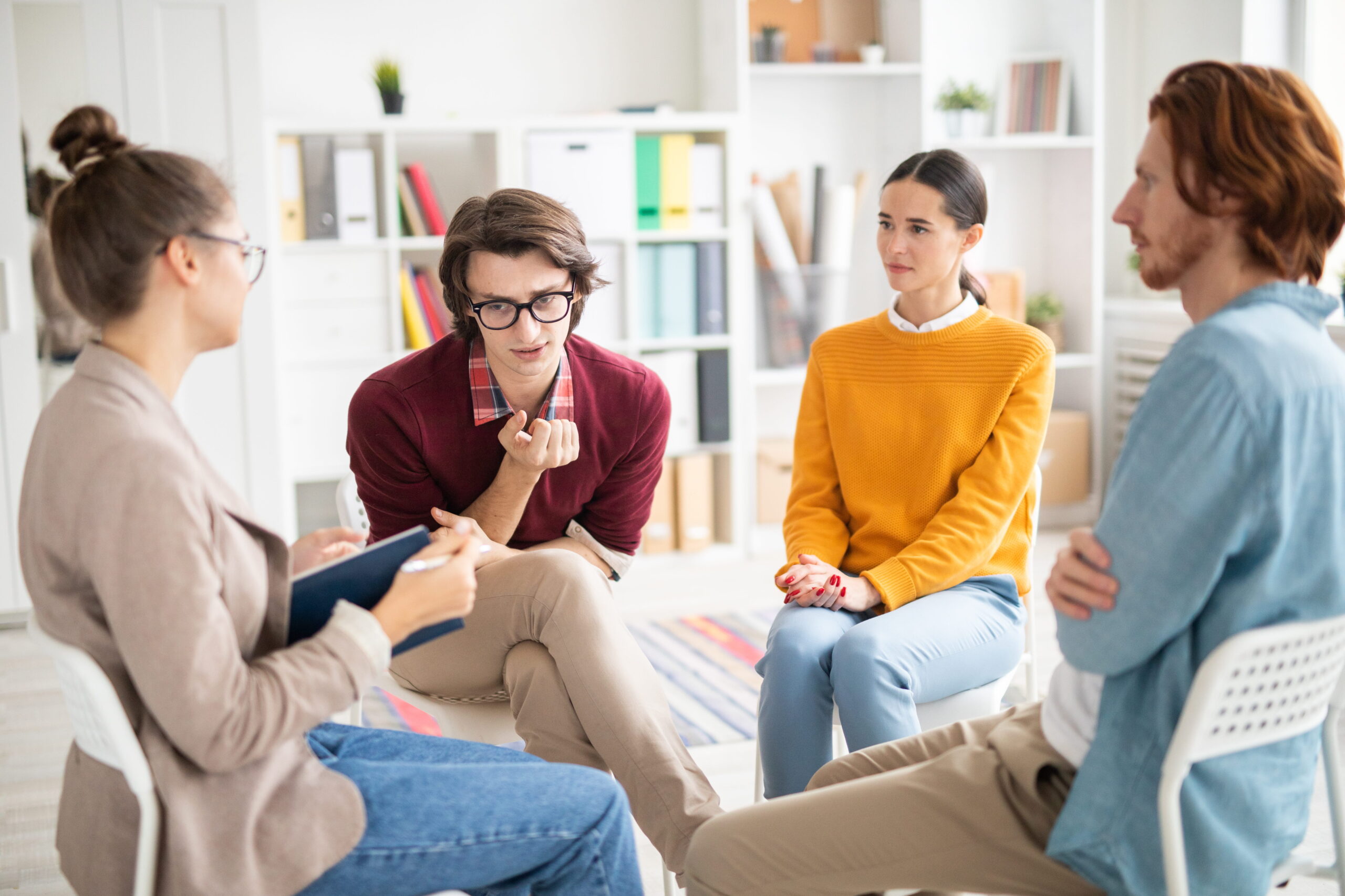 Four coworkers sit in a bright office forming a circle and discussing around a low table