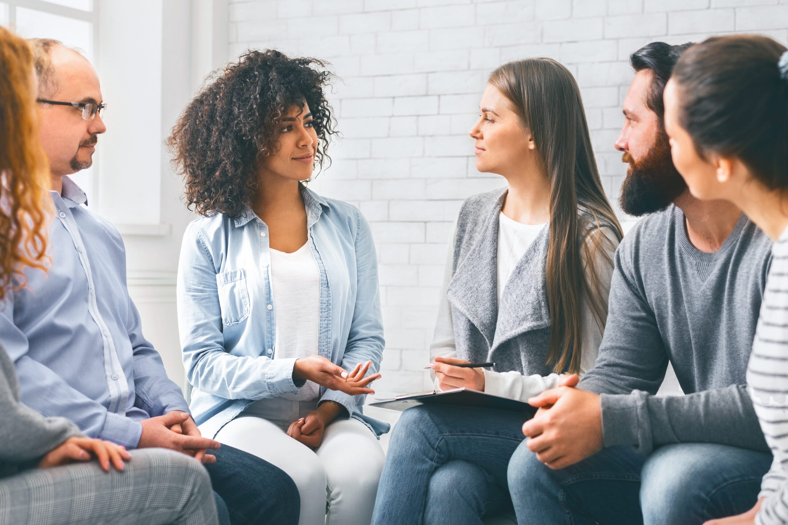 Diverse team members sit in a circle and discuss ideas in a bright office environment